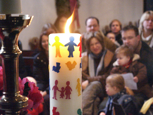 Kerze mit bunten Menschenkindern vor Familien mit ihren Kindern